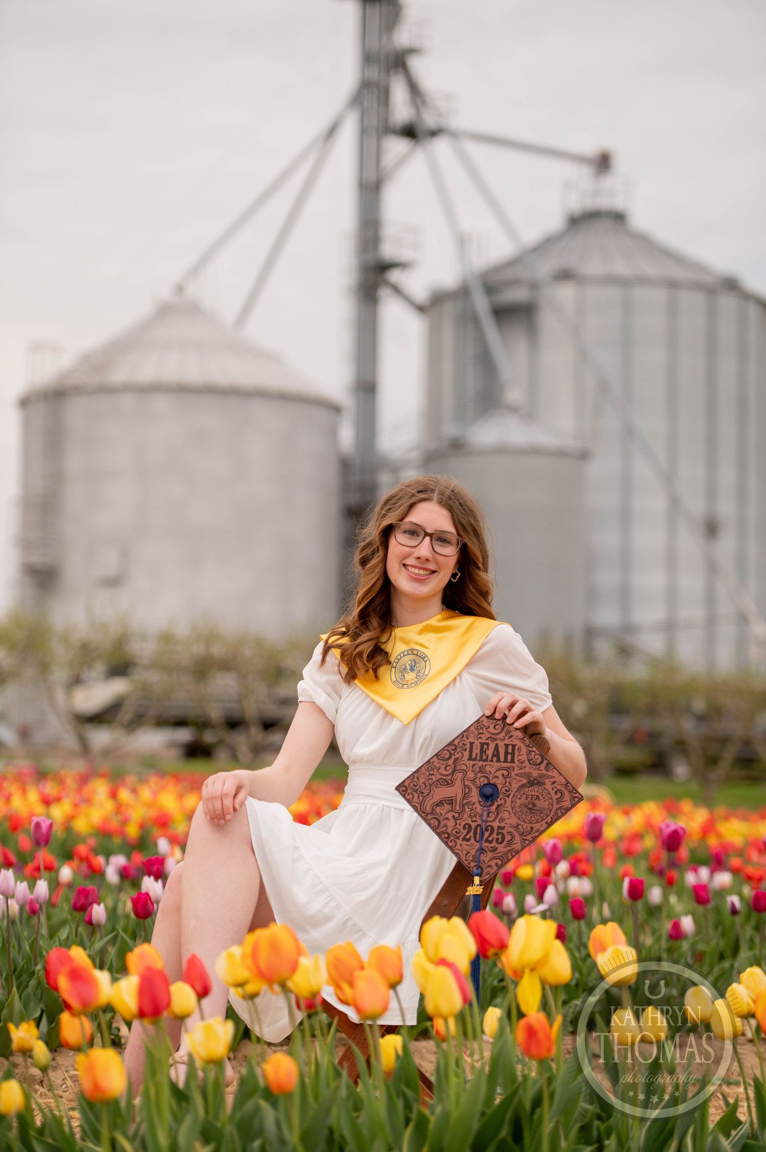 A graduation photo in a vibrant tulip field with grain silos in the background.