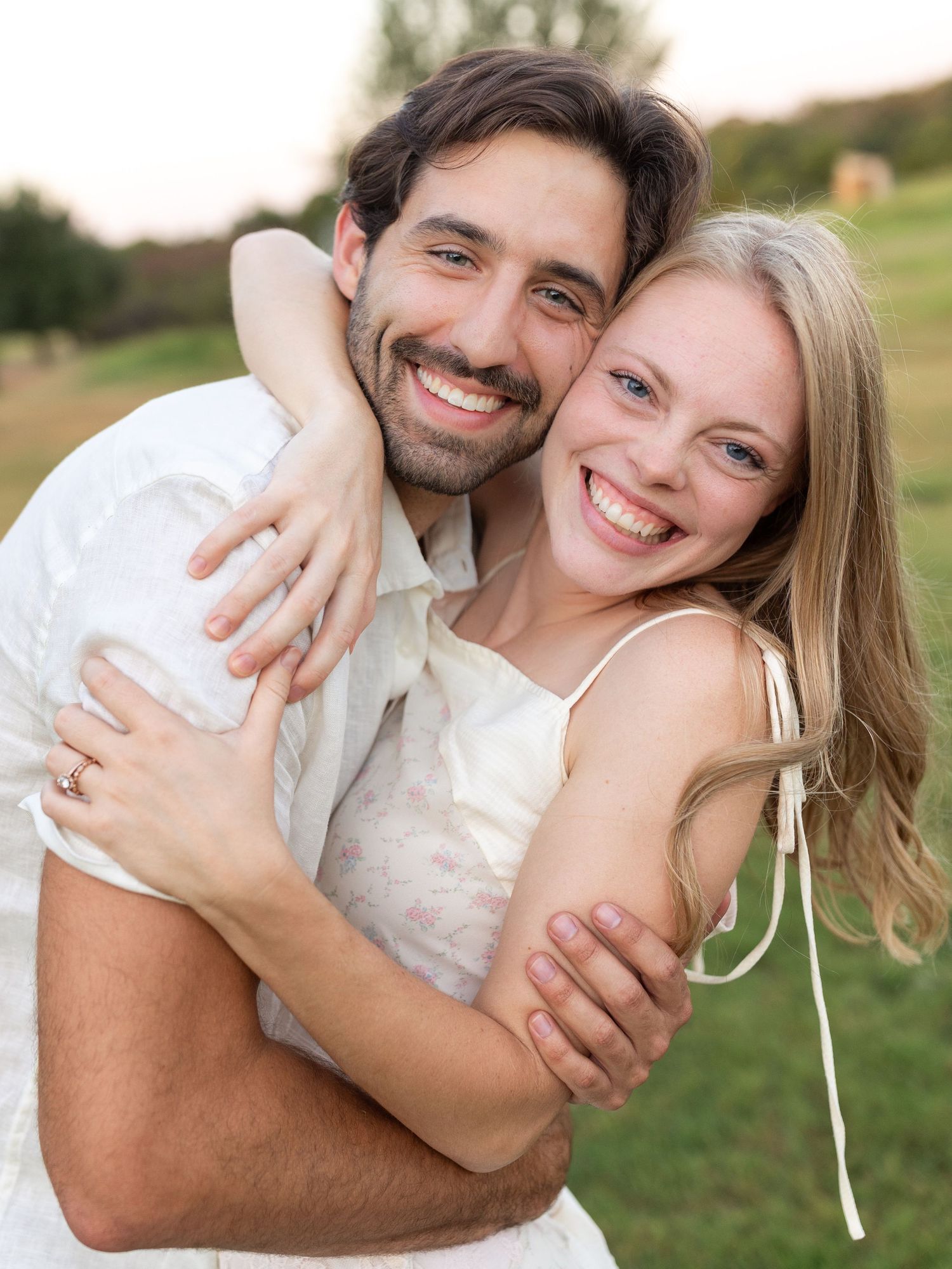 A couple embraces in warm sunlight against a desert mountain backdrop wearing neutral-colored clothing in a romantic pose.