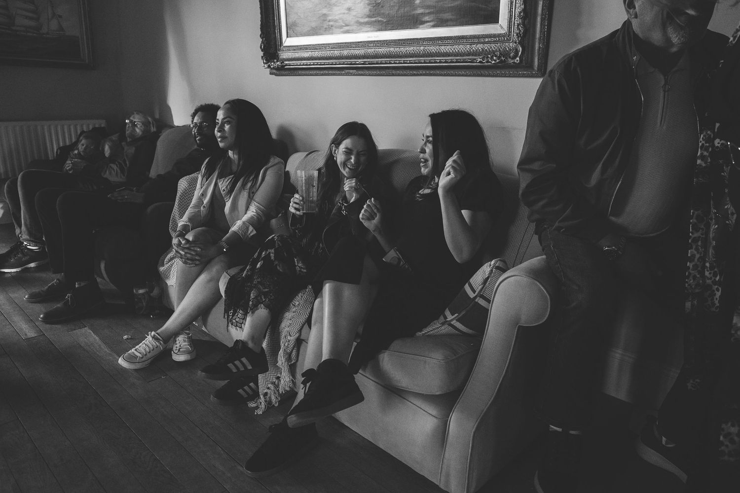 A group of people sit on a couch together in a dimly lit room, captured in black and white photography.