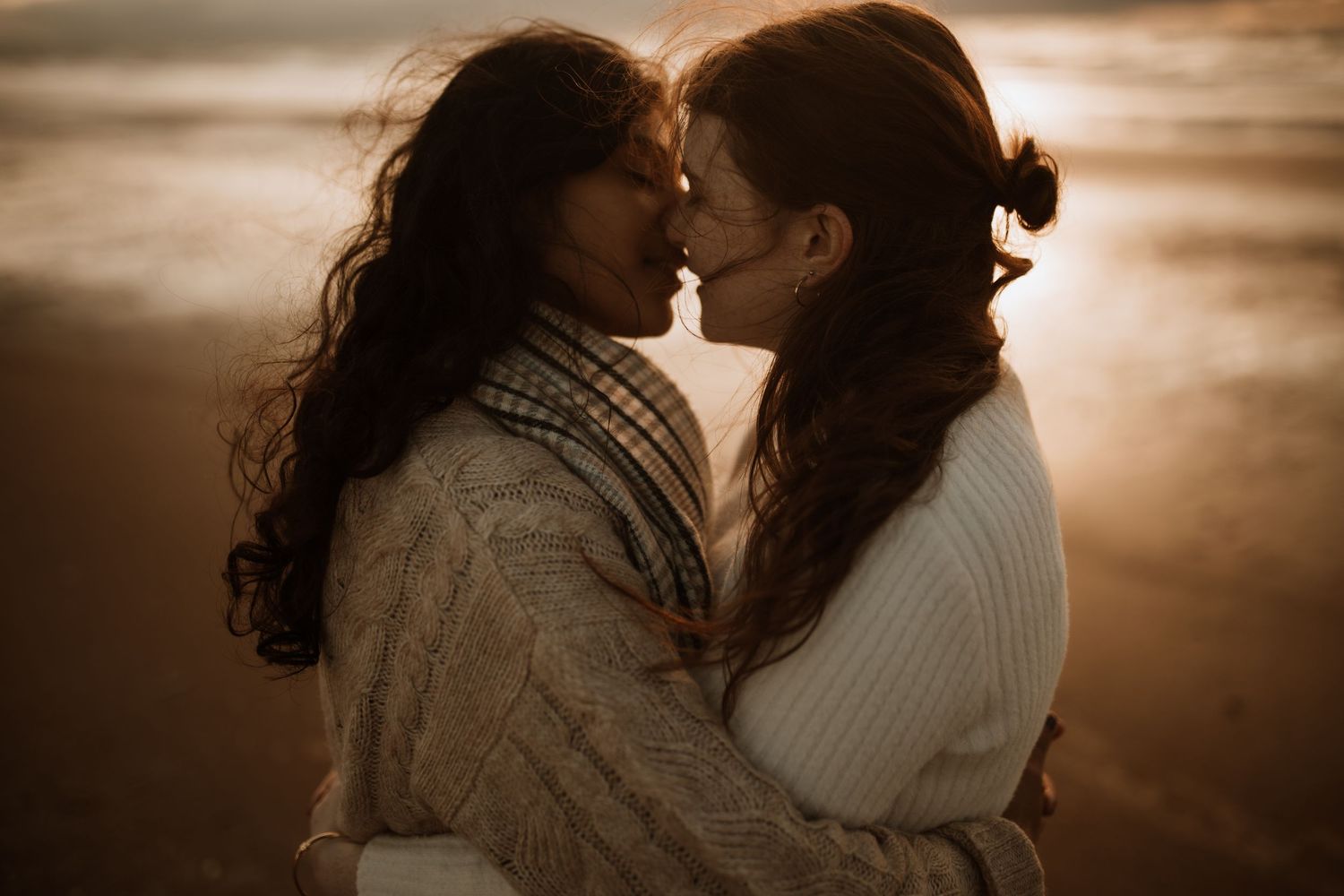 A tender romantic moment between two people in cozy sweaters silhouetted against a warm sunset sky.