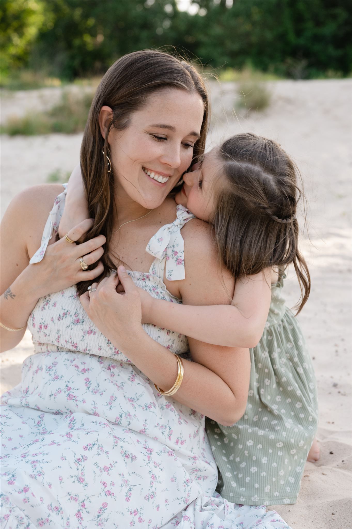A tender moment between parent and child sitting on sandy ground, wearing floral and polka dot dresses.