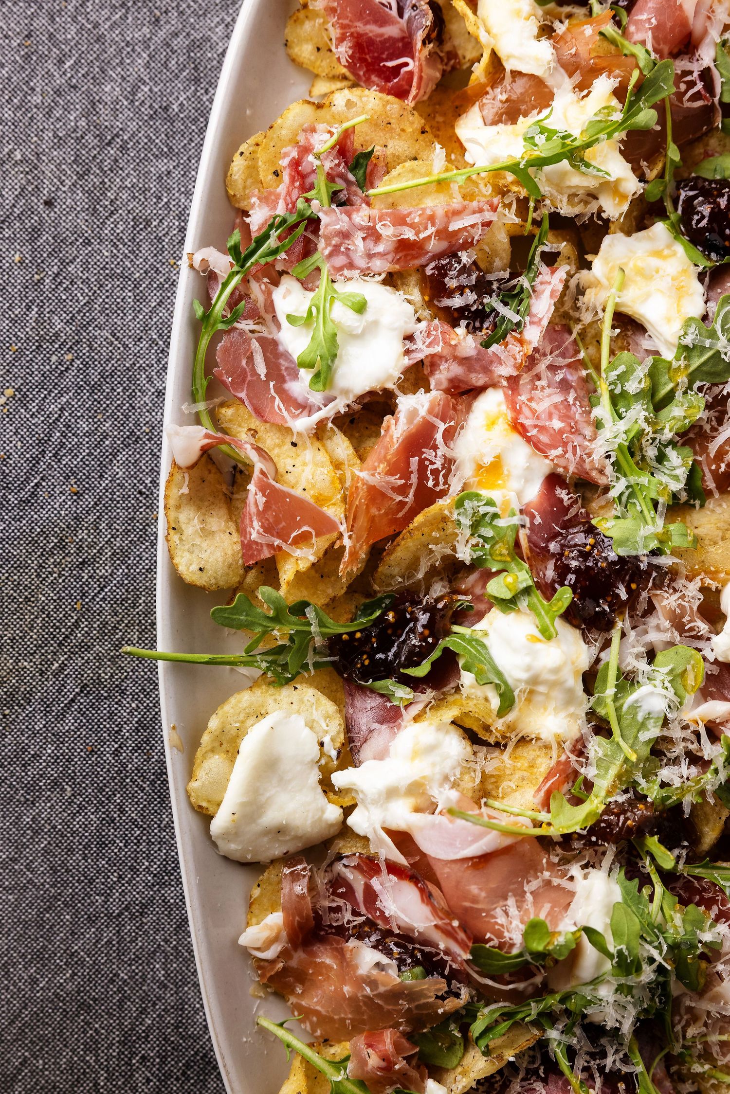 A platter of crispy smashed potatoes topped with prosciutto, burrata, arugula, and shaved parmesan cheese.