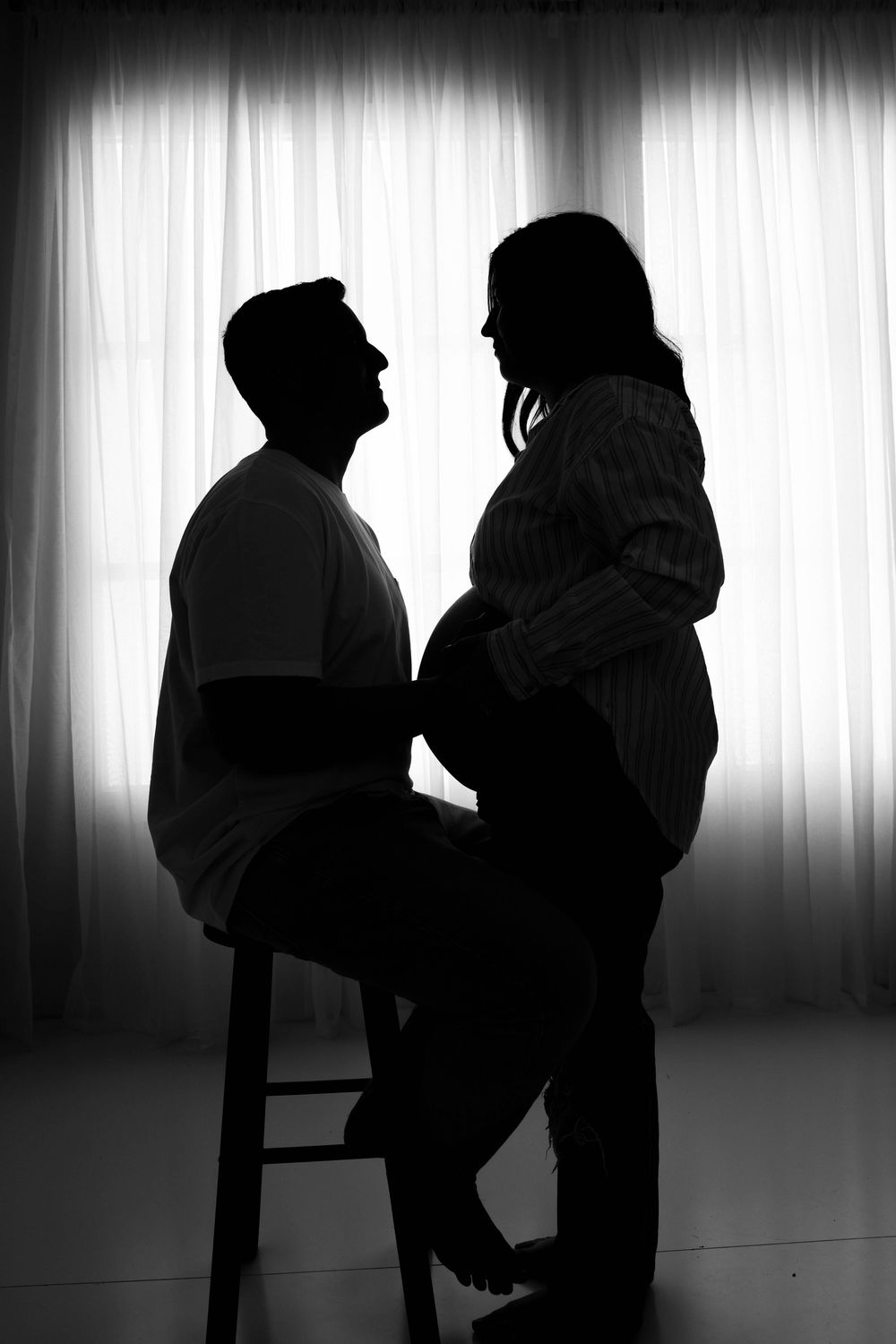 Artistic black and white silhouette of a couple in an intimate pose against backlit curtains.