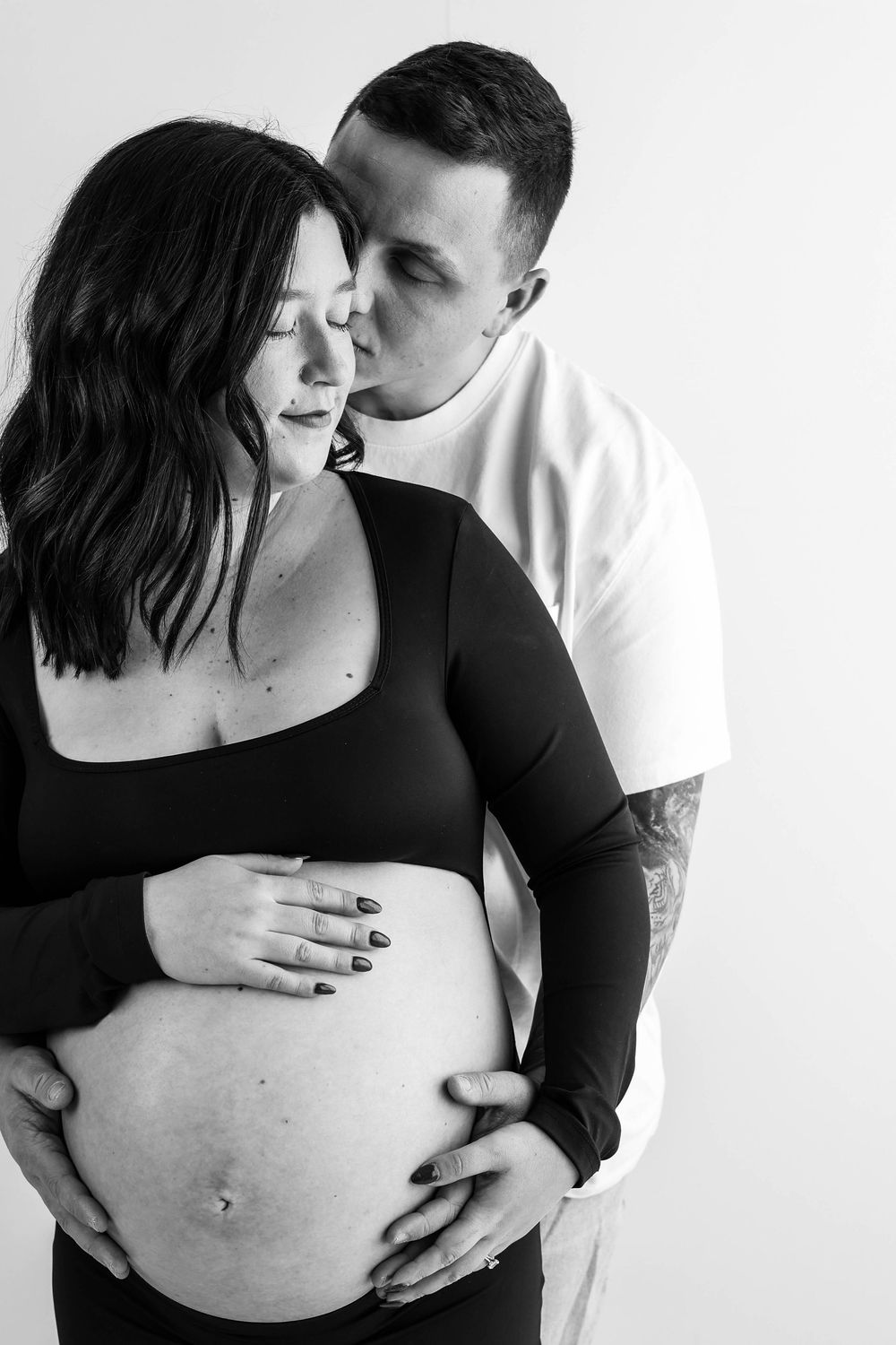 A black and white maternity photo shows an intimate moment between a couple as they embrace the pregnant belly.