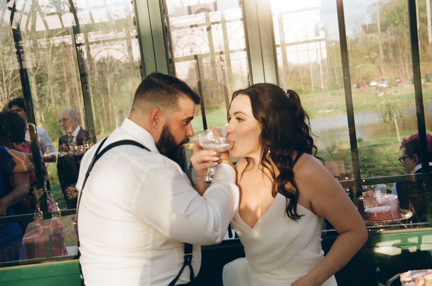 A bride and groom share a playful moment feeding each other cake during their greenhouse wedding reception.