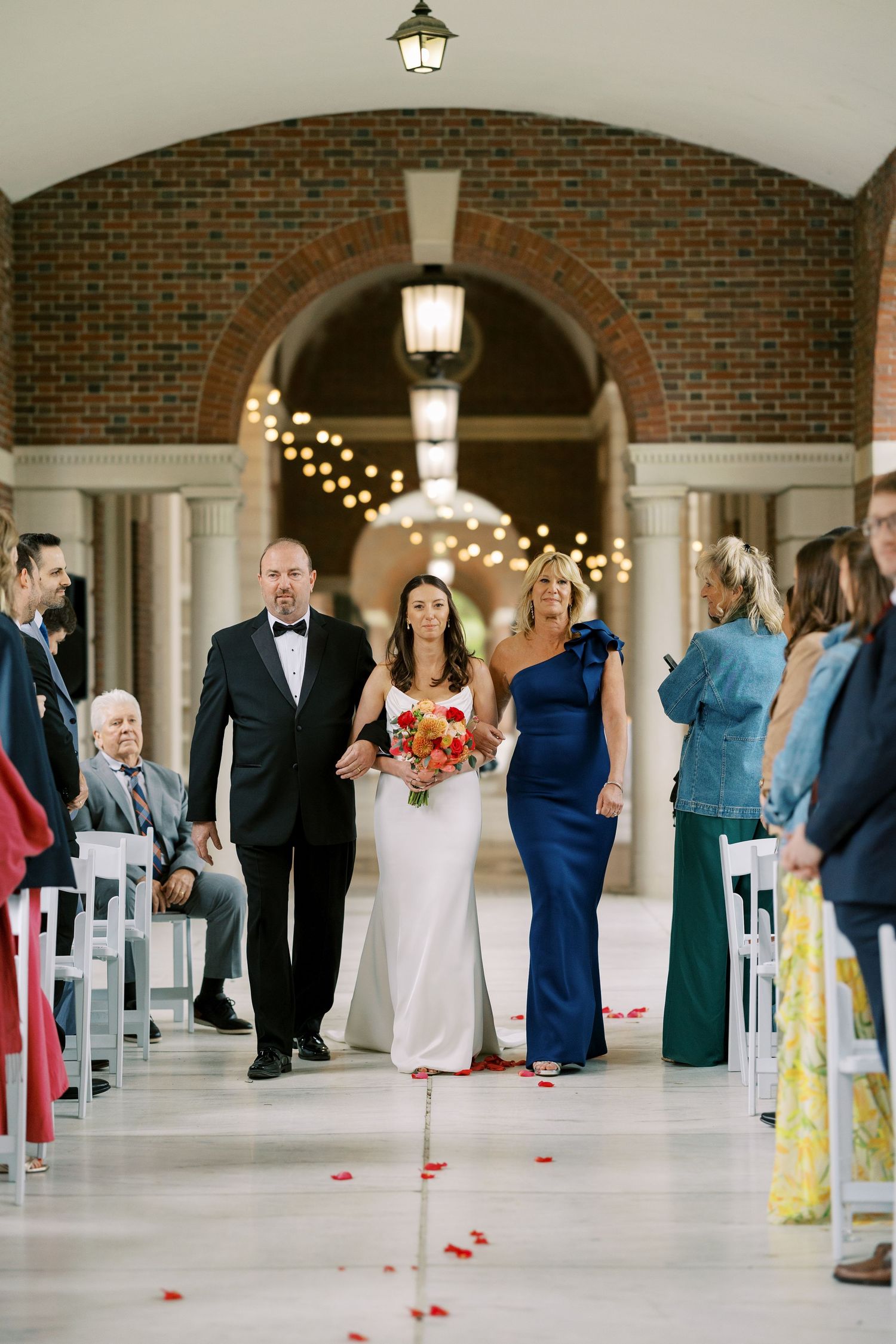 Wedding ceremony processional in an elegant brick archway corridor with lanterns and string lights overhead at Hall of Springs.
