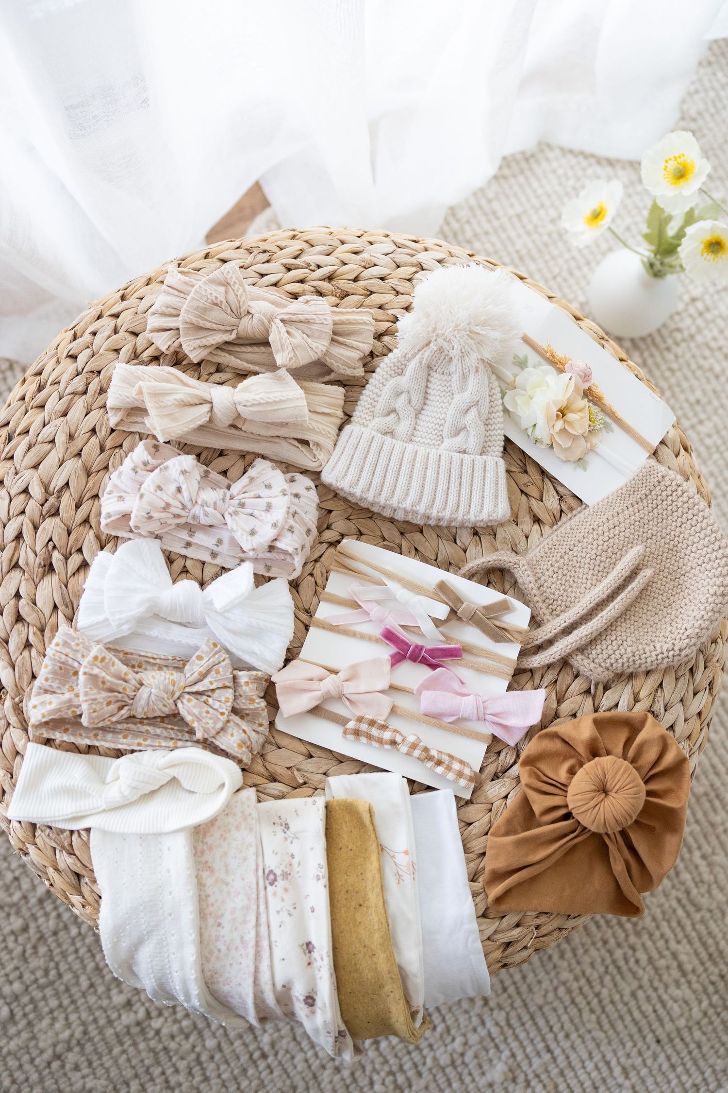 A collection of neutral-toned baby accessories including bows, headbands, hats and hair clips arranged on a woven placemat.