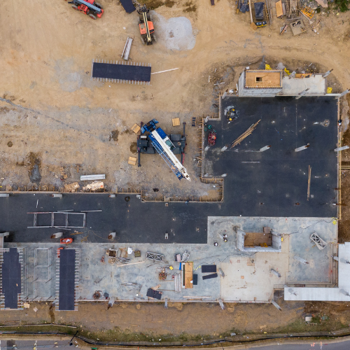 Aerial view of a construction site with asphalt paving and vehicles on sandy ground, captured from directly above.