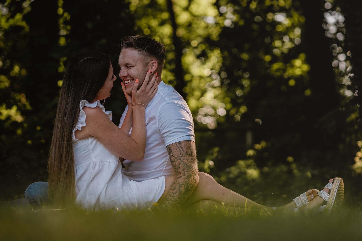 Intimate outdoor portrait of a couple sitting together in a sunlit forest setting.