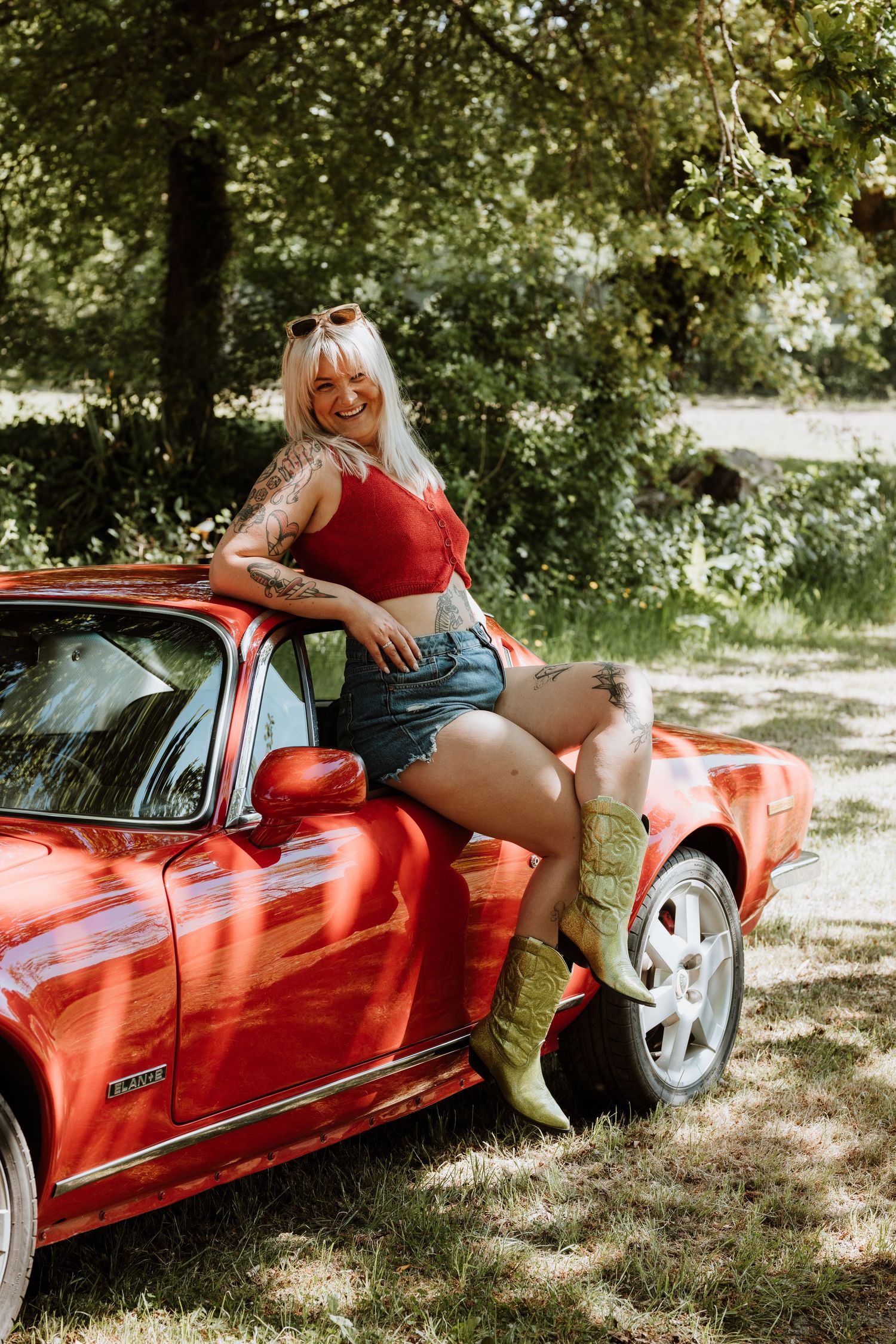 Vintage red sports car parked in a scenic wooded area on a sunny summer day.