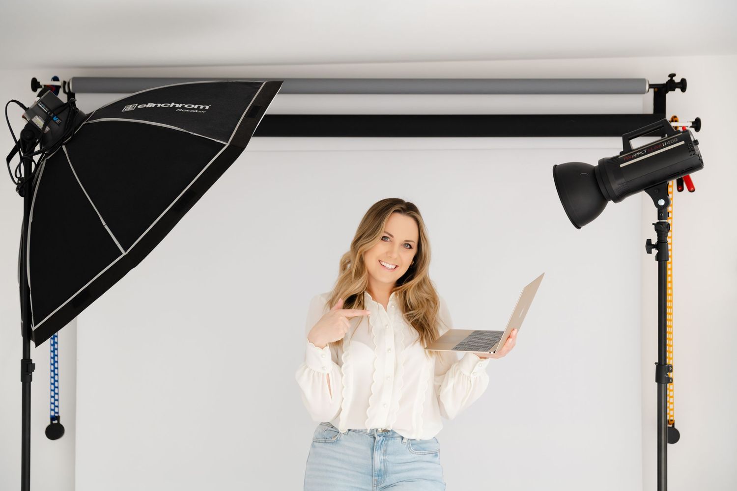 Professional photography studio setup with softbox lighting, backdrop, and person posing against white background.