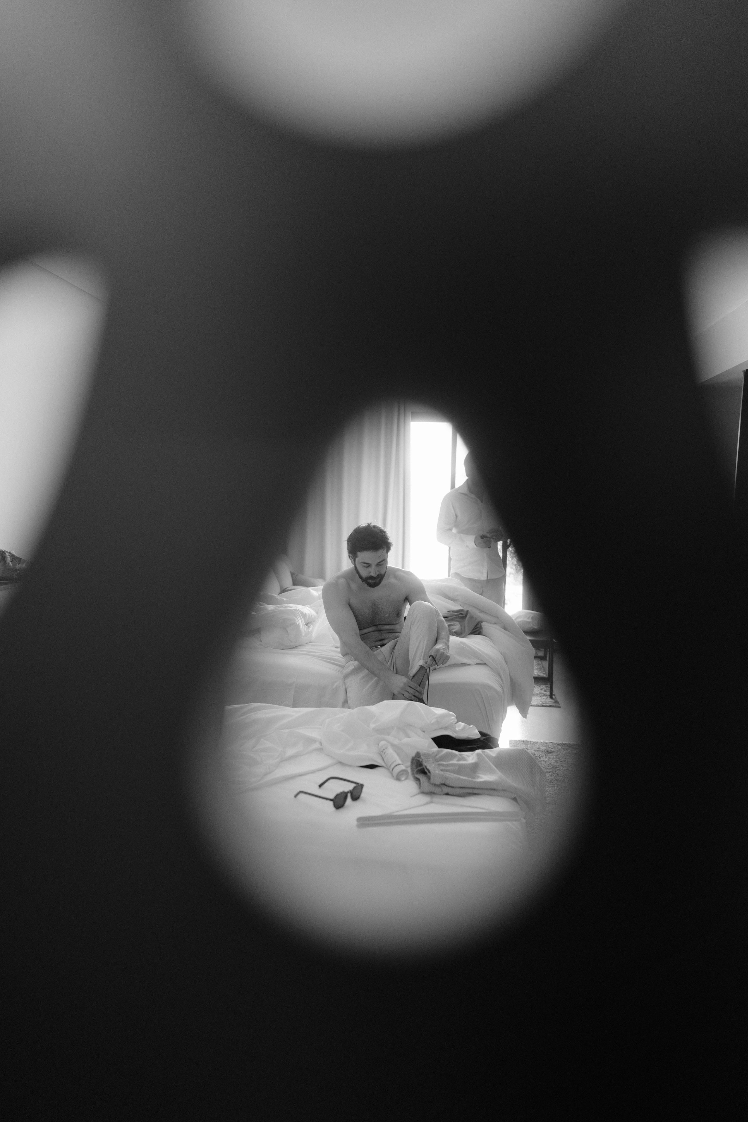A black and white artistic photo taken through an opening showing preparation on a bed.