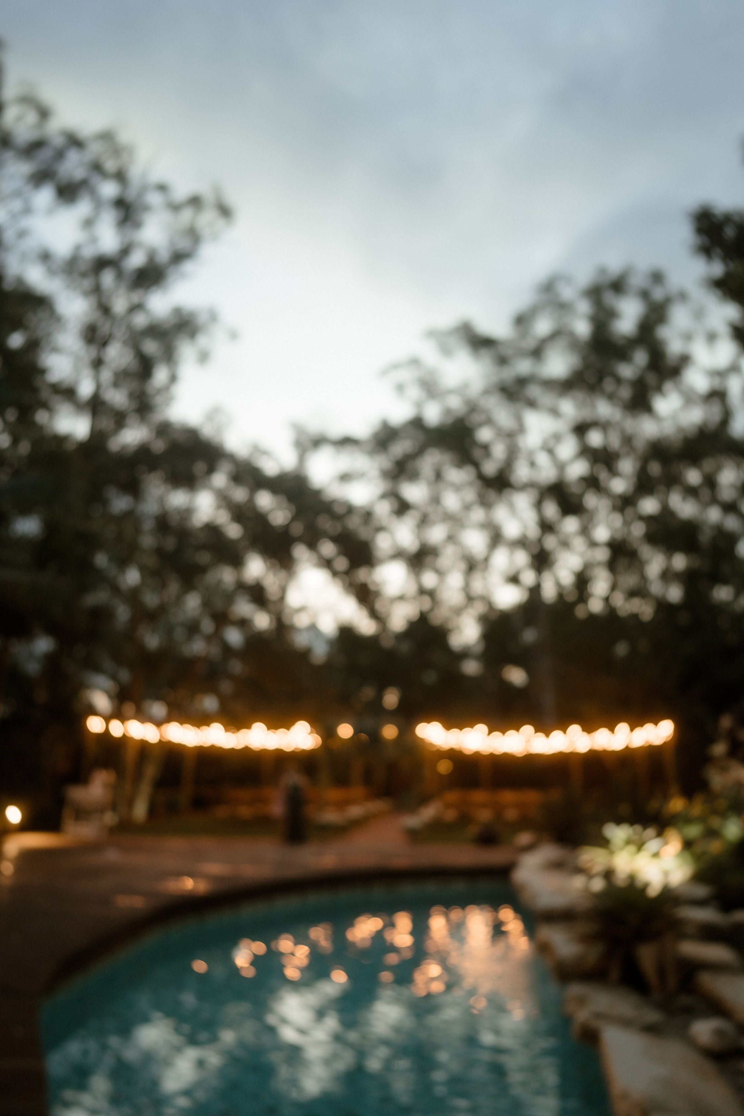 String lights illuminate an outdoor swimming pool at dusk creating a romantic ambiance.