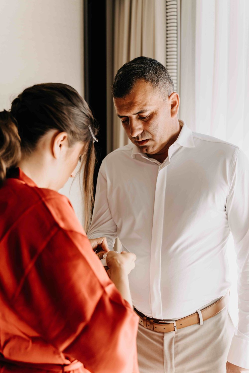 Four sequential images show two people in white and orange garments interacting in soft window lighting.
