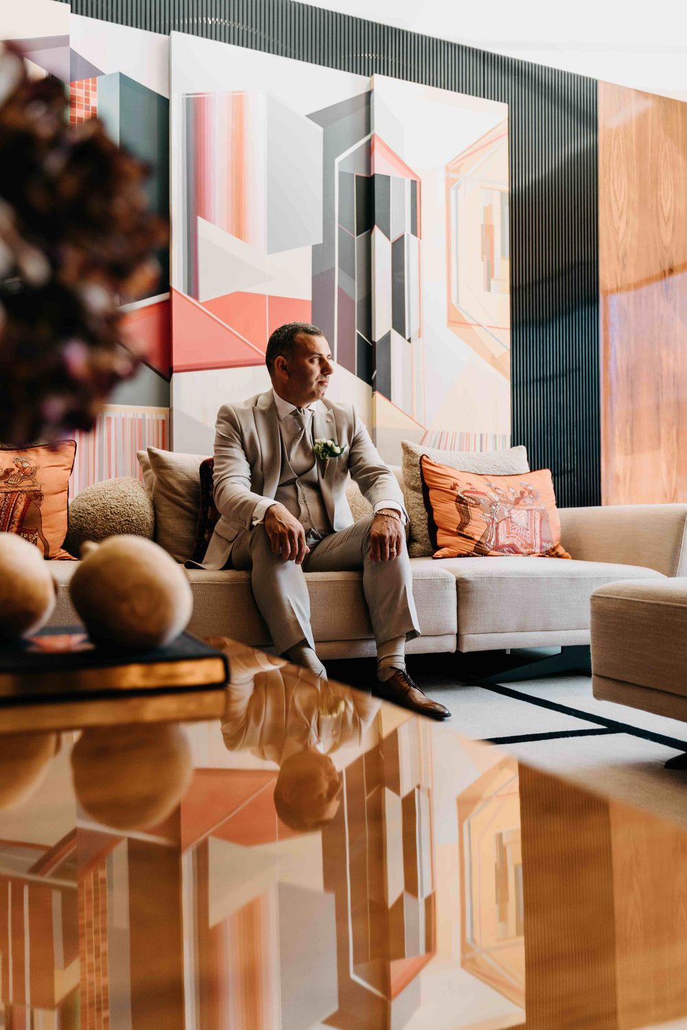 Modern living room interior with geometric wall art and reflective flooring features a person in a light suit on a sofa.