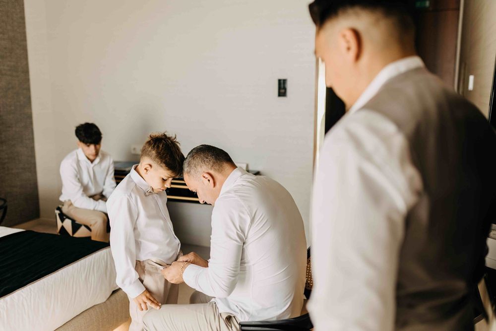 People in formal white and gray attire getting ready in a minimalist hotel room interior.