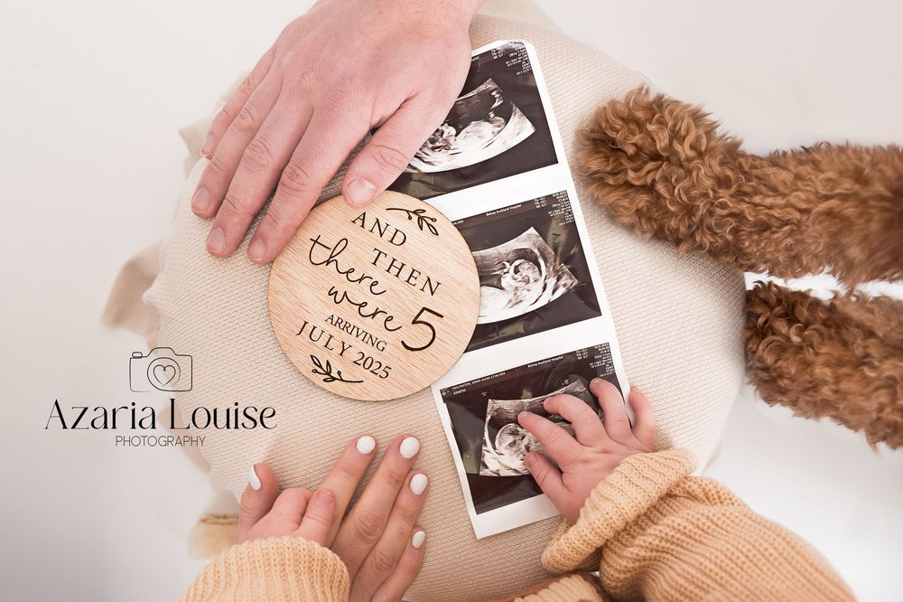 Hands holding ultrasound photos and a wooden disc announcing pregnancy alongside a teddy bear.