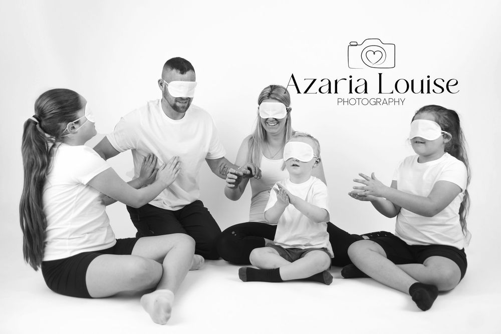 A family group sits together on the floor wearing matching white tops and black bottoms, as they laugh and interact.