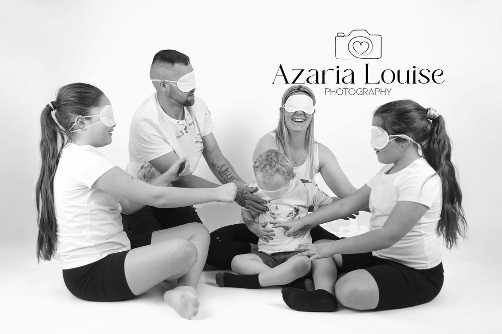 A group of four people in white shirts sitting on a floor in a circle during a professional black and white photo session.