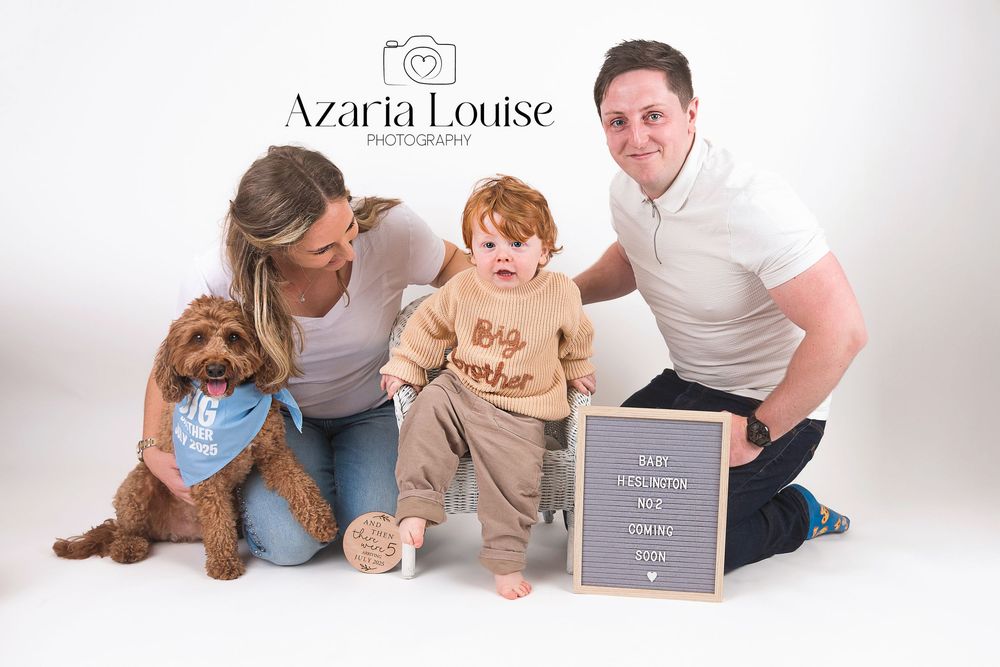 A family poses together in a studio setting with their brown labradoodle dog and a chalkboard sign.