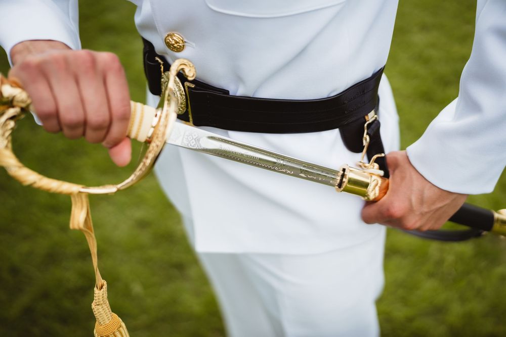 A close-up view of hands holding a ceremonial military sword with gold accents against a white uniform.