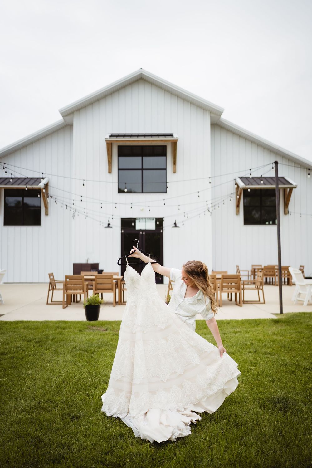 A white modern farmhouse wedding venue with string lights and a flowing white dress twirling in the foreground.
