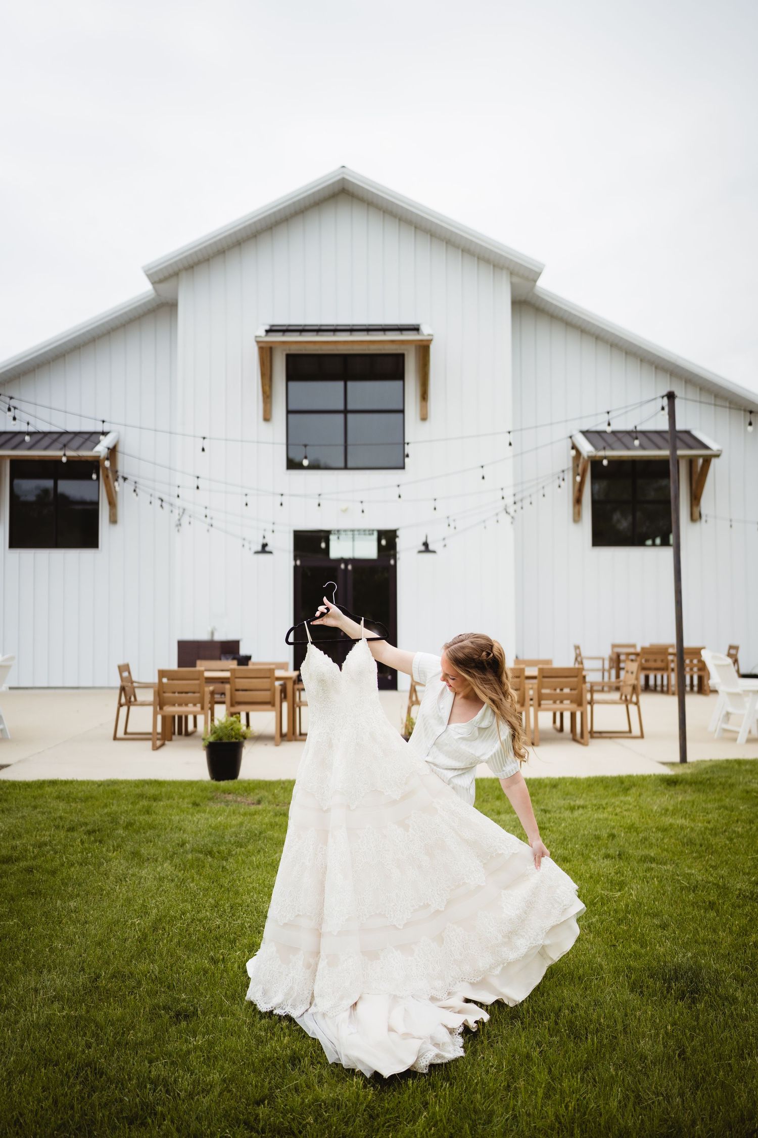 A white modern farmhouse wedding venue with string lights and a flowing white dress twirling in the foreground.