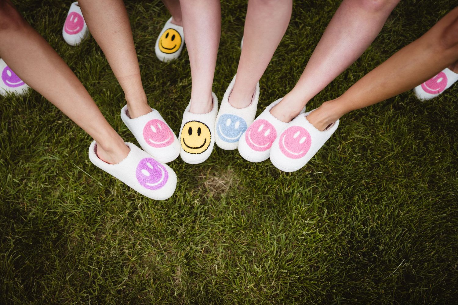 Pink and yellow smiley face decorated shoes arranged in a circle on green grass.