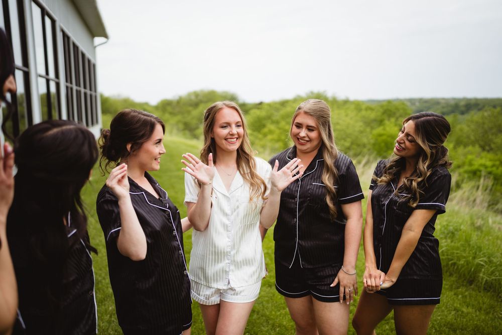 A group of friends in contrasting black and white outfits laugh together while standing in a grassy outdoor setting.