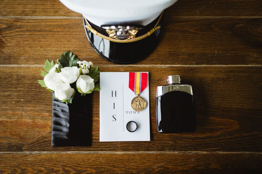 Wedding accessories including rings, flowers, medals, and invitations arranged on a rustic wooden table surface.