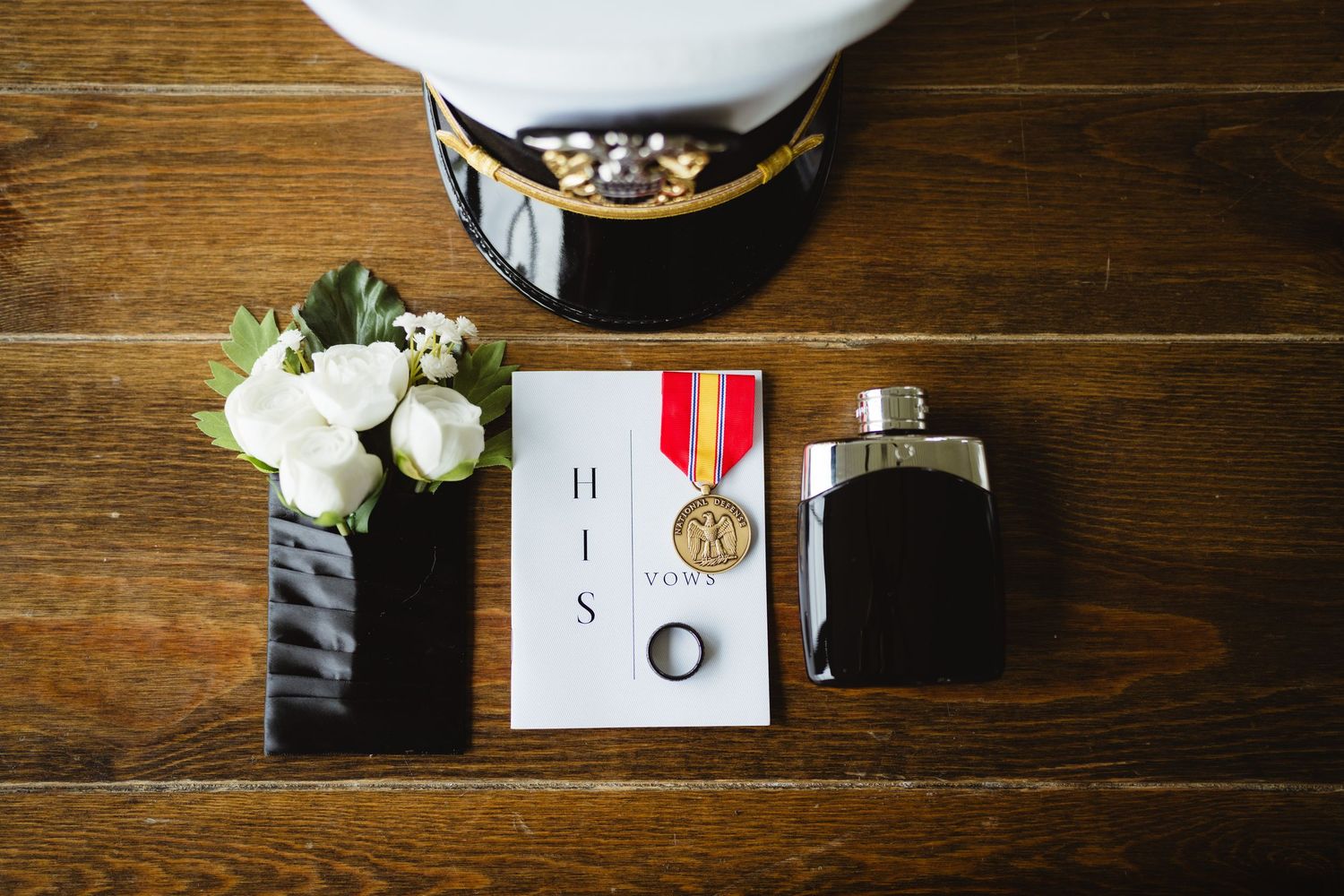 Wedding accessories including rings, flowers, medals, and invitations arranged on a rustic wooden table surface.