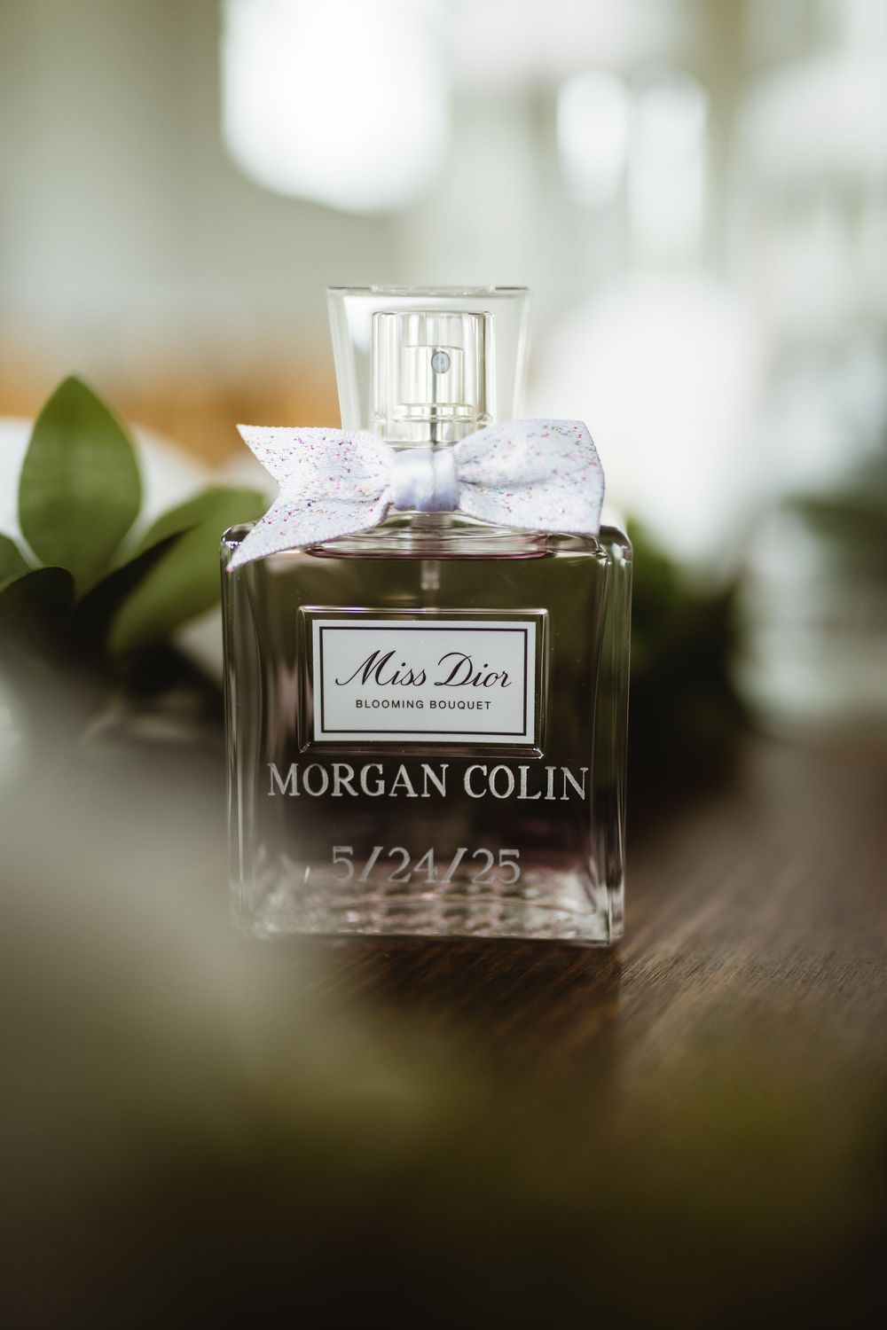 A personalized Miss Dior perfume bottle with a white bow and 'Morgan Colin' engraved, sitting on a wooden surface.