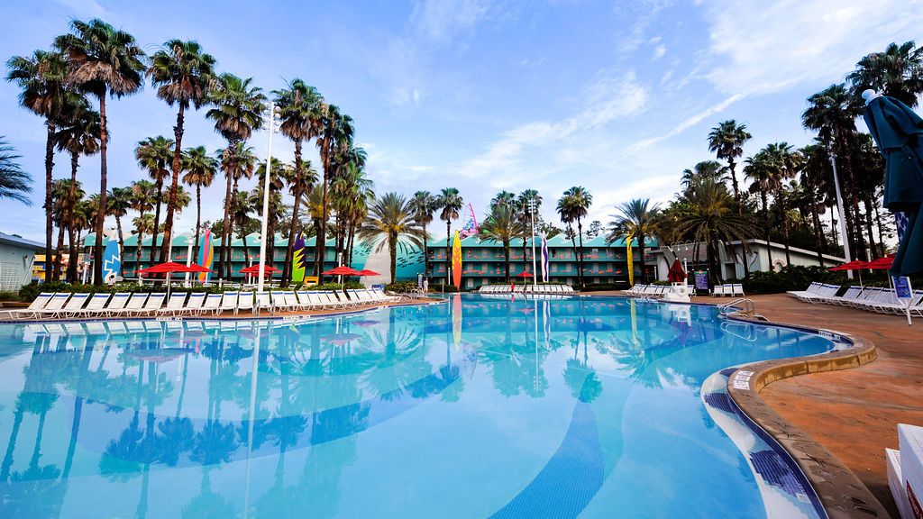 Resort swimming pool surrounded by tall palm trees under blue sky at Disney's All-Star Sports Resort.