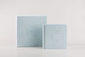 Two light blue square minimalist albums or portfolios with simple embossed details displayed against a white background.