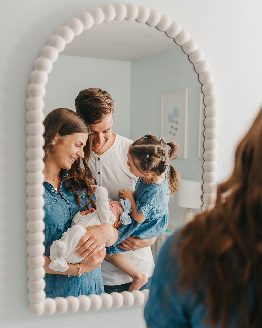 Mirror reflection shows a family gathered around a newborn baby in a bright, modern nursery setting.