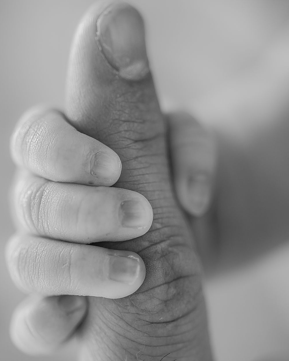 Close-up black and white photo of a tiny baby hand grasping an adult finger