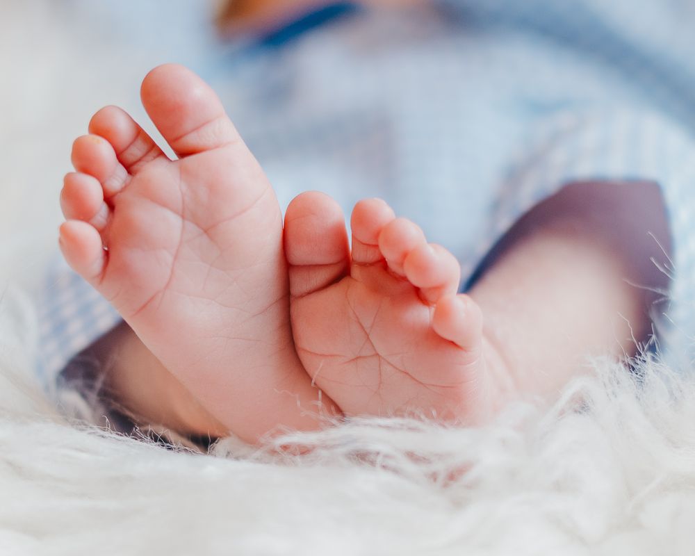 A series of tiny newborn baby feet in soft focus resting on delicate white fabric texture.