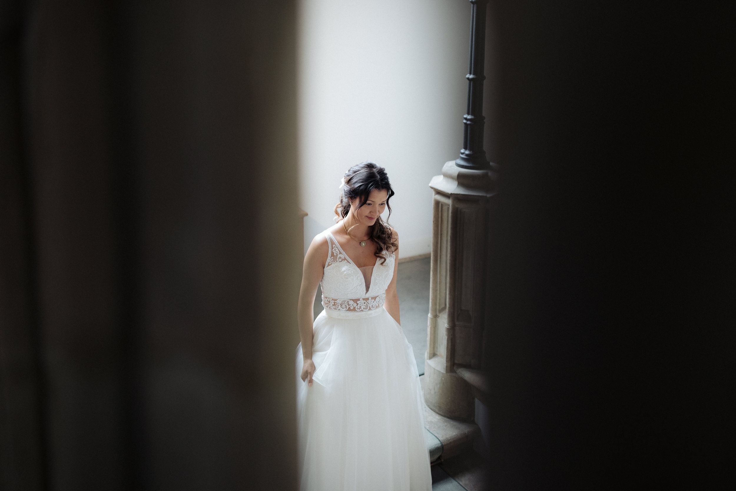 A bride in an elegant white wedding dress poses against a dark background near dramatic door lighting.