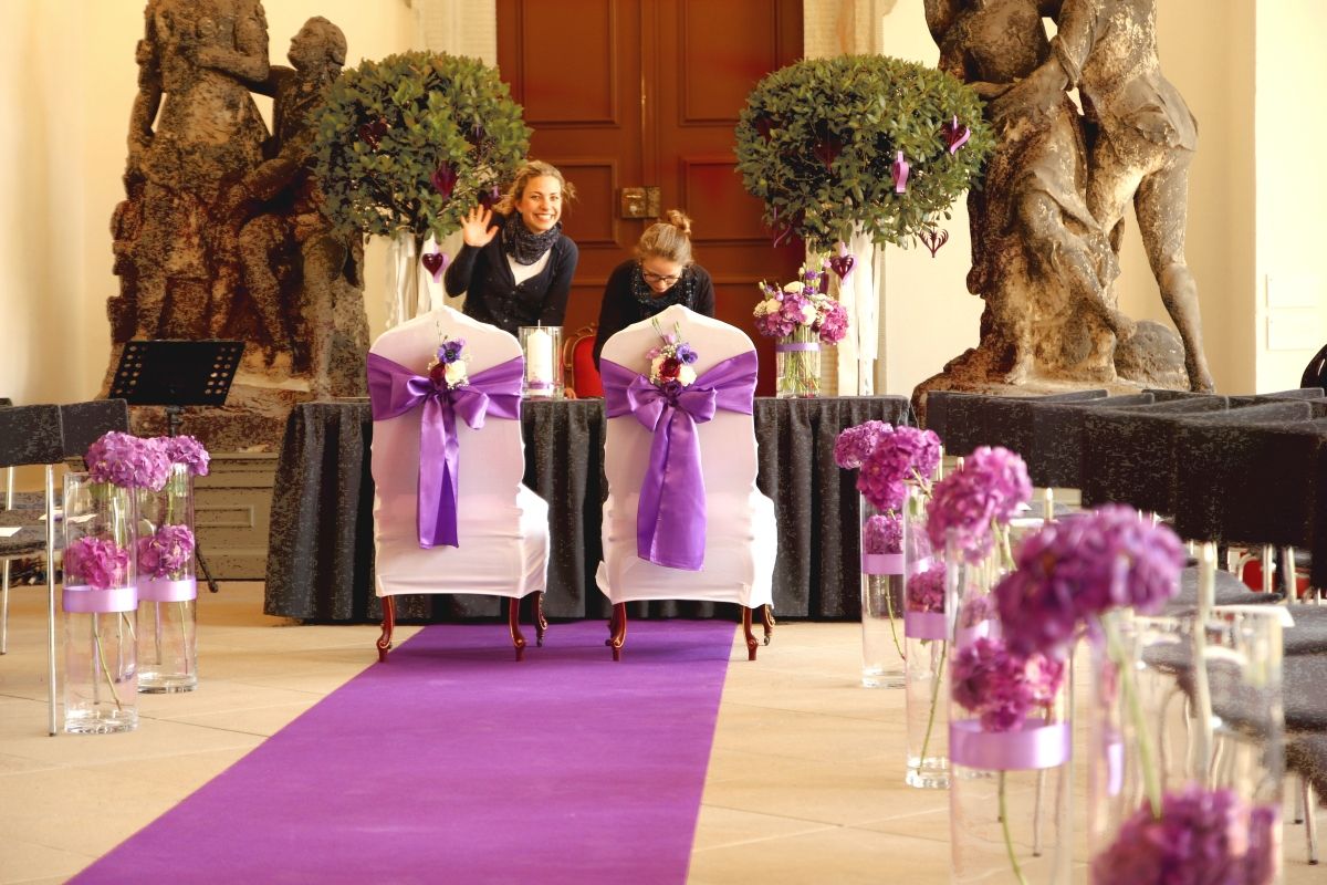 Purple-themed wedding ceremony setup with ornate aisle decorations featuring glass vases and floral arrangements.