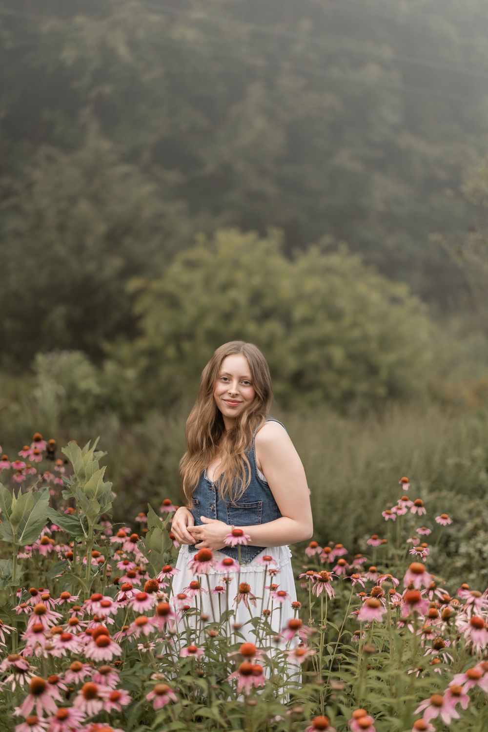 Someone stands in a blooming garden filled with pink coneflowers on a misty summer day.