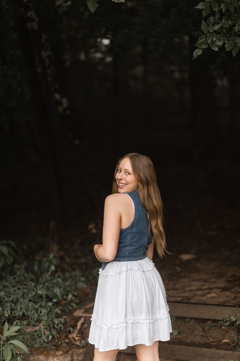 Along a shaded woodland path with dense foliage, a blue and white dress sways in gentle motion.