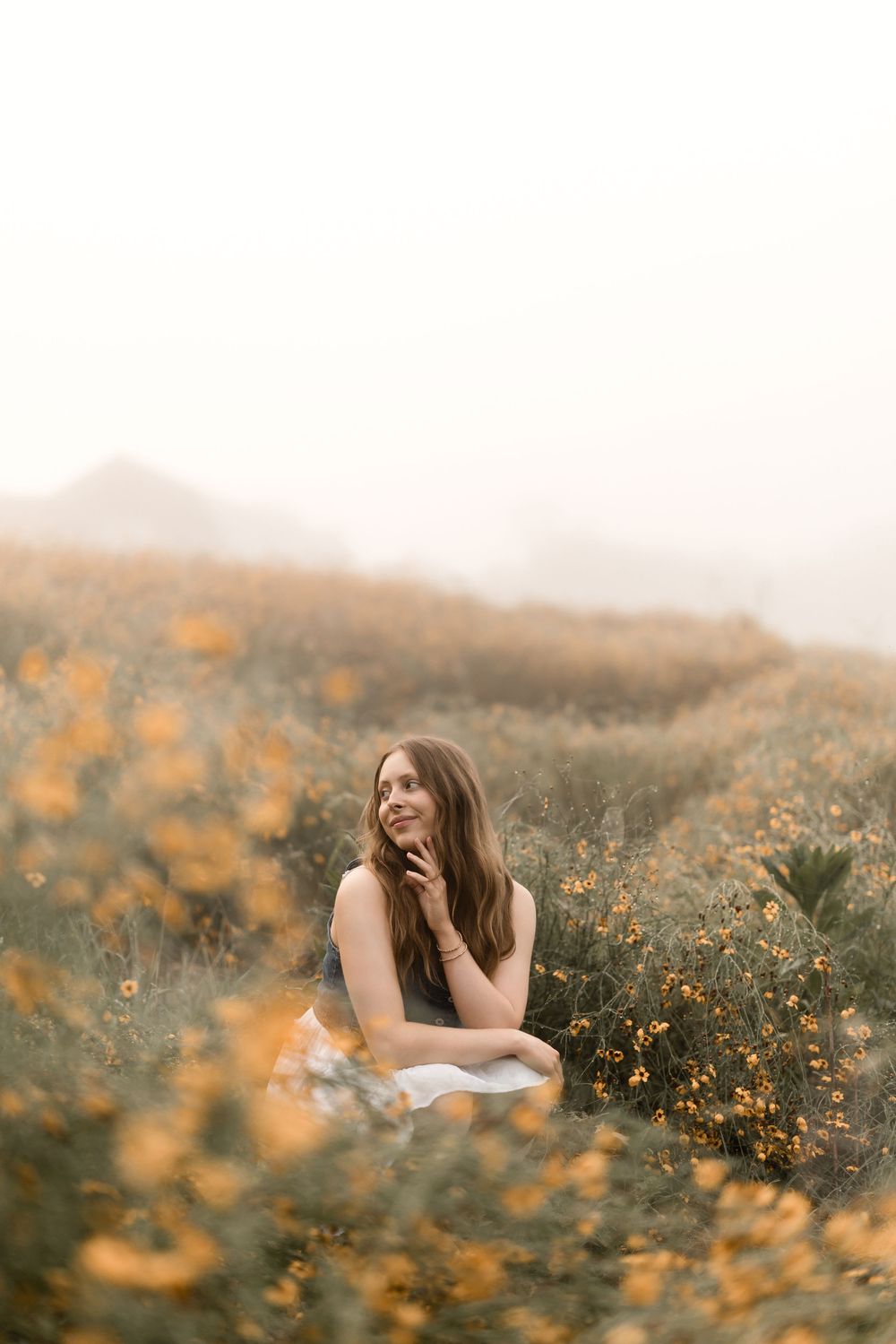 A person sits in a dreamy field of orange wildflowers at sunset with soft mist in the background.