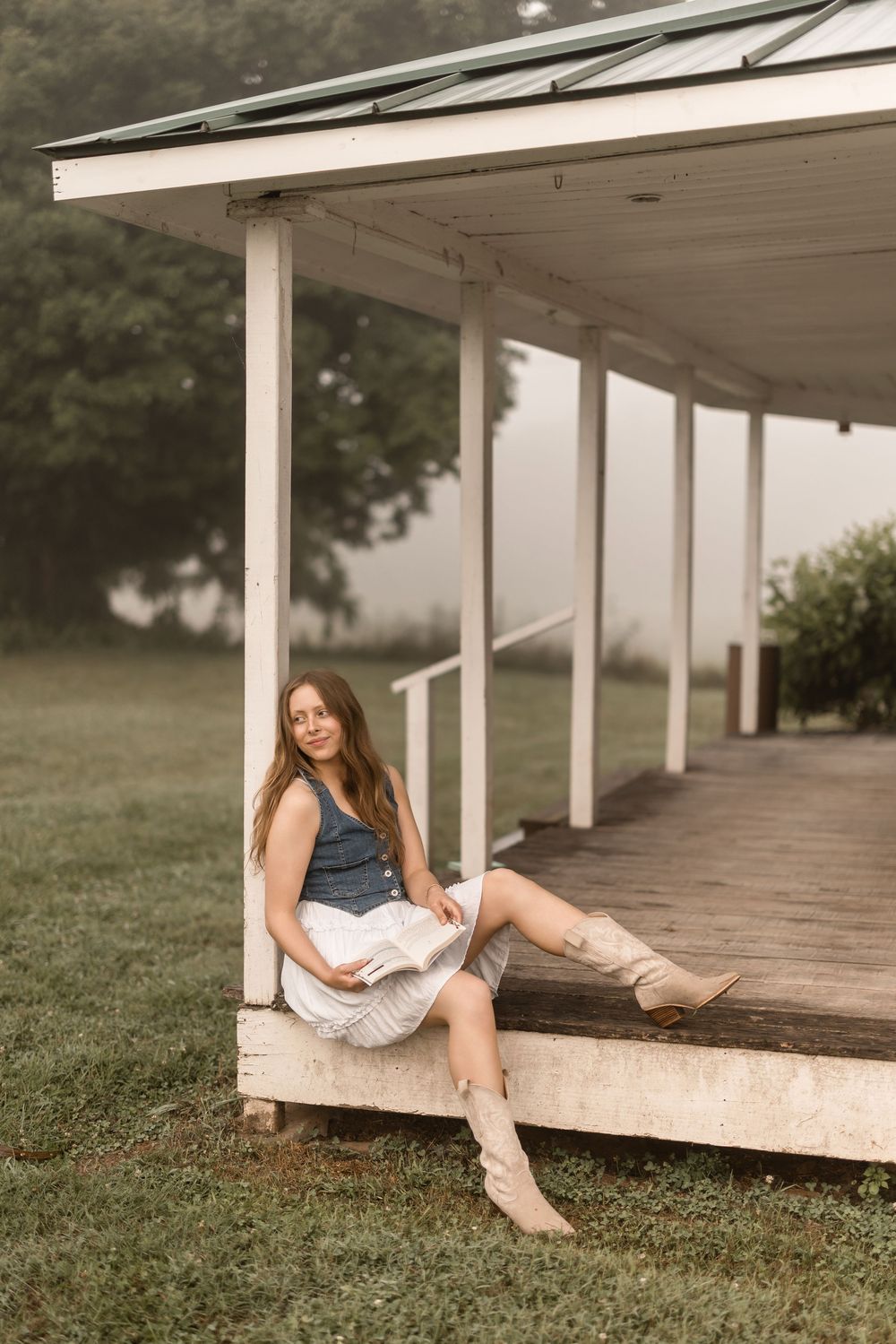 A figure reclines on a white porch deck surrounded by grass in a dreamy summer scene.