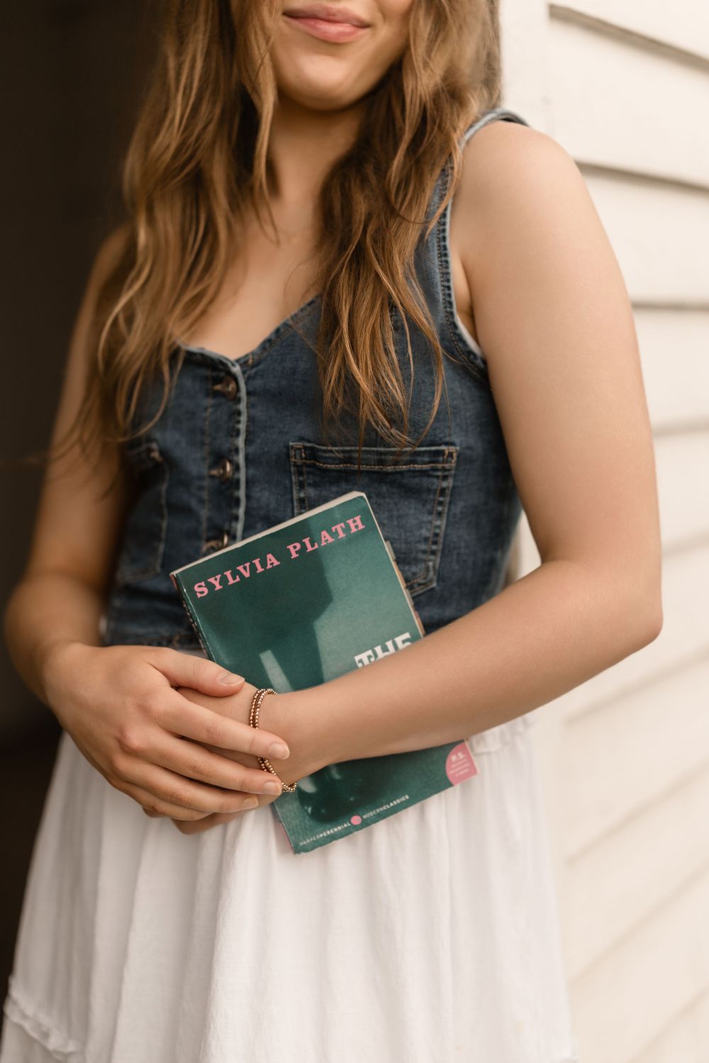 Woman in denim top holding green book against white backdrop in casual lifestyle photo series.