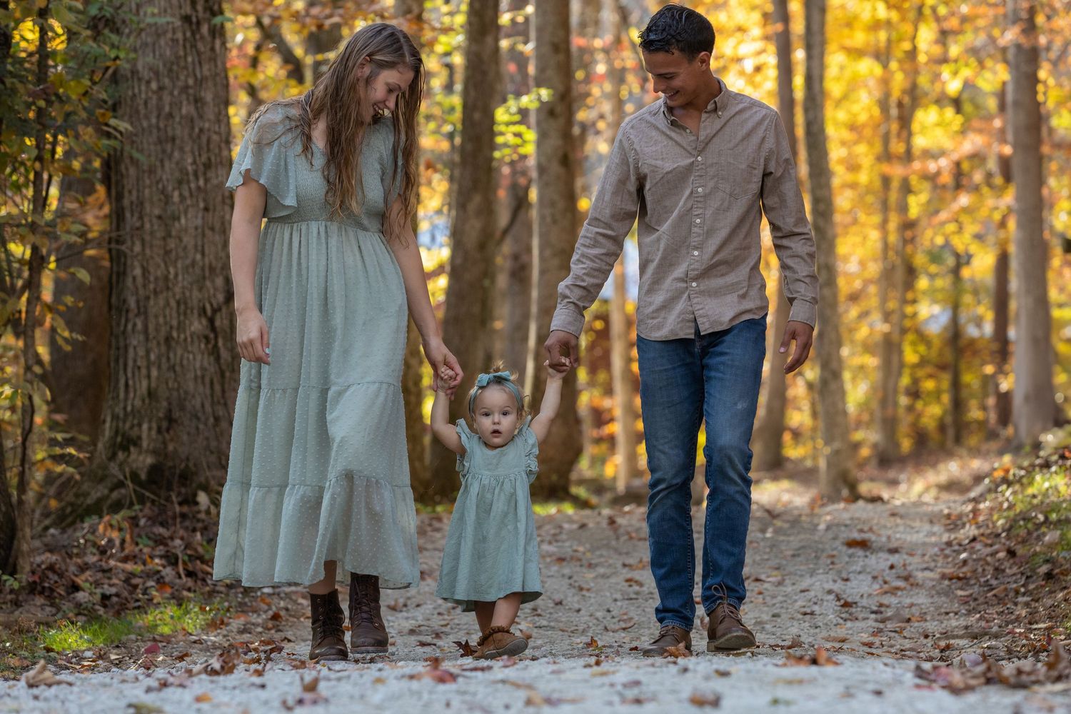 A family walks together holding hands along a wooded trail during a golden autumn afternoon.