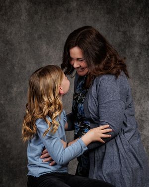 A woman and young girl share a warm embrace and smile at each other in a professional studio portrait.