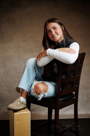 Figure rests on a wooden chair in contrasting light and shadow against a brown background.