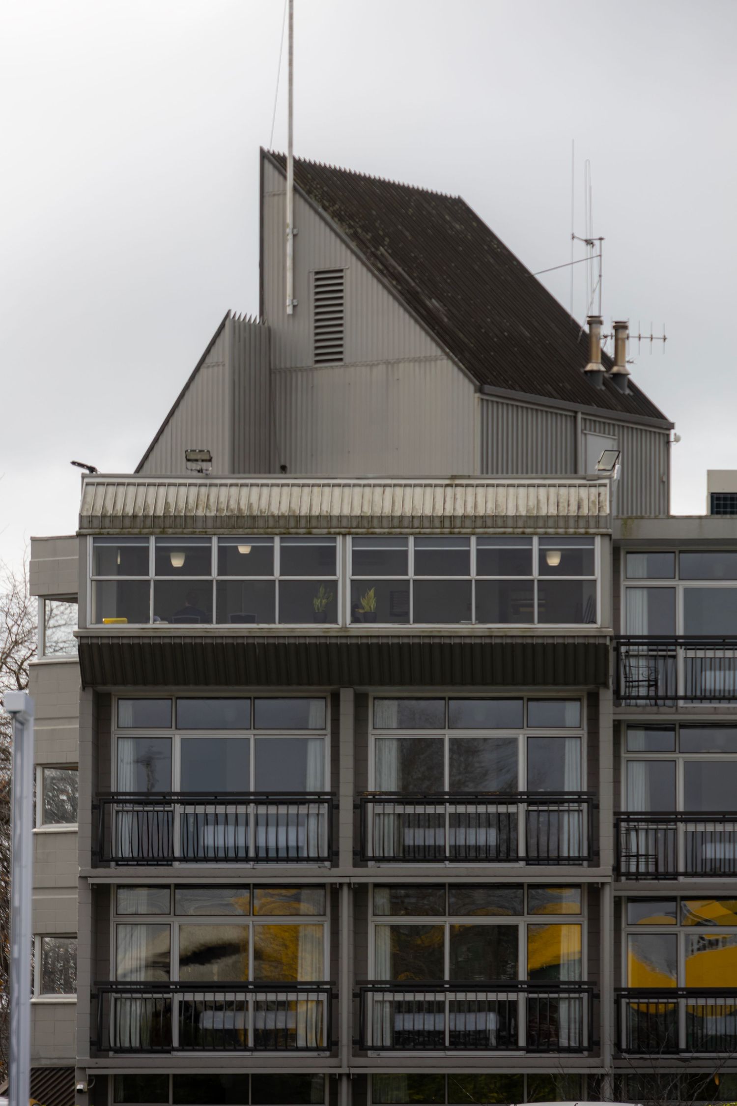 Retro-modern office building with a steep, angled rooftop and a collage of glass balconies and antennas.