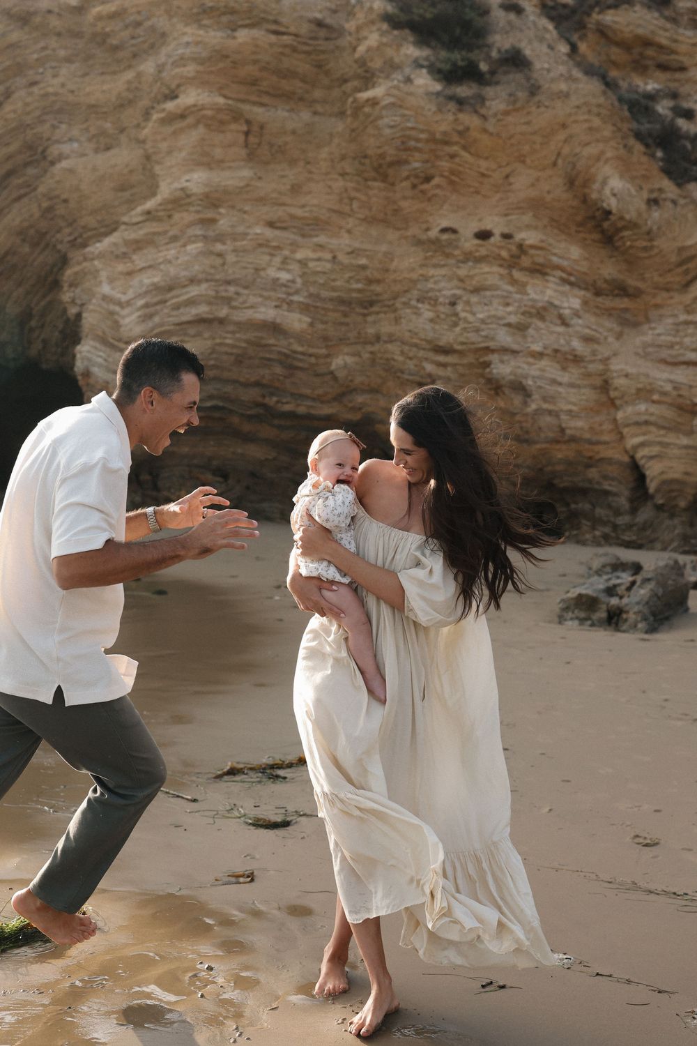 A family shares a joyful moment together on a scenic beach with rocky cliffs in the background.