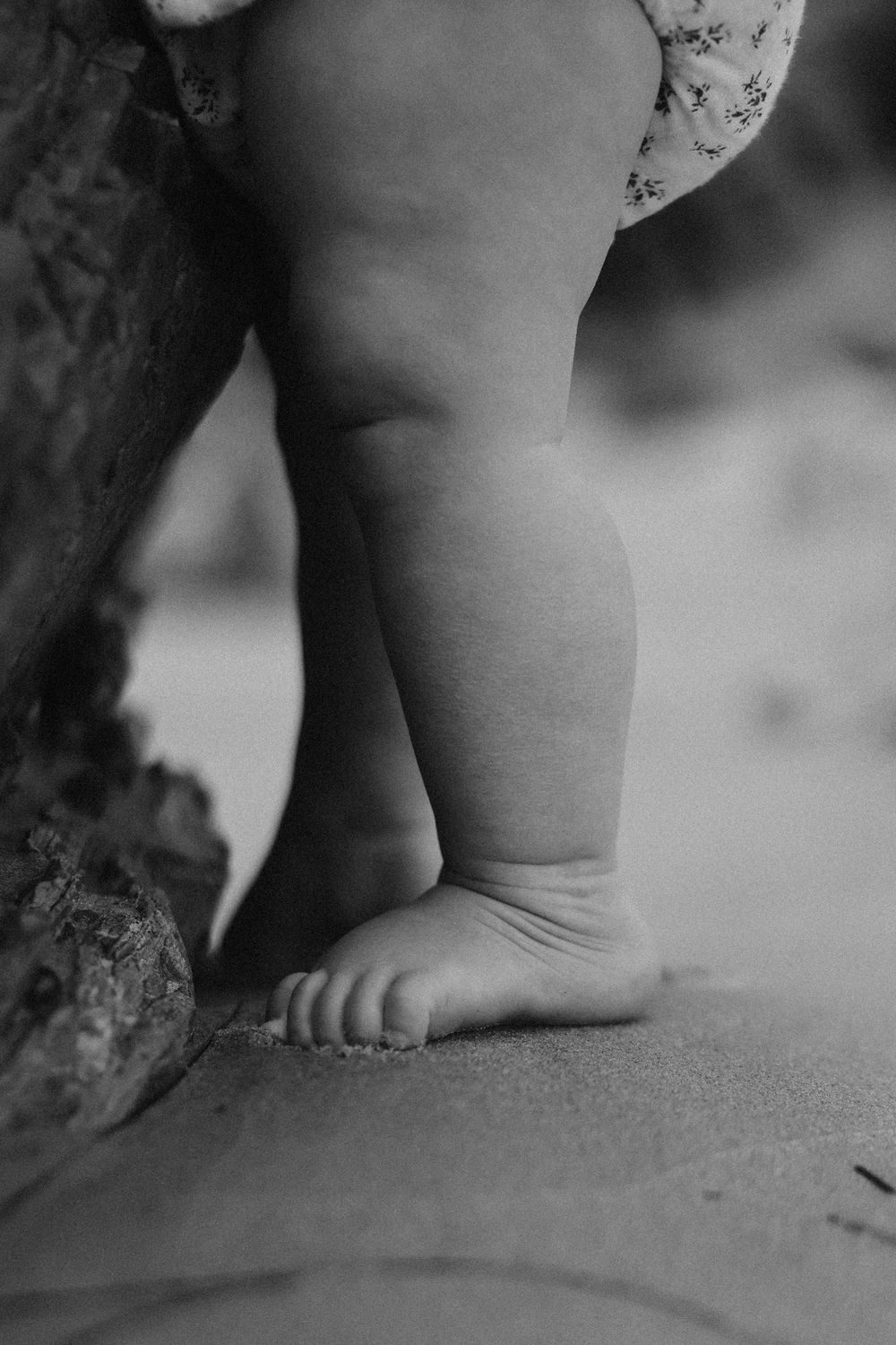 Close-up black and white image of a baby's chubby foot resting against a textured surface.